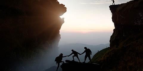 Male hiker celebrating success on top of a mountain in a majestic sunrise and Climbing group friends helping hike up.