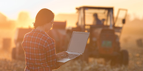 A student on a laptop computer, with a tractor behind her