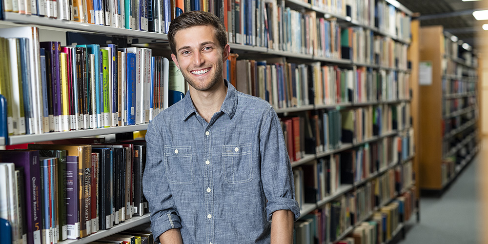 A teenage man, standing in front of a shelf full of books