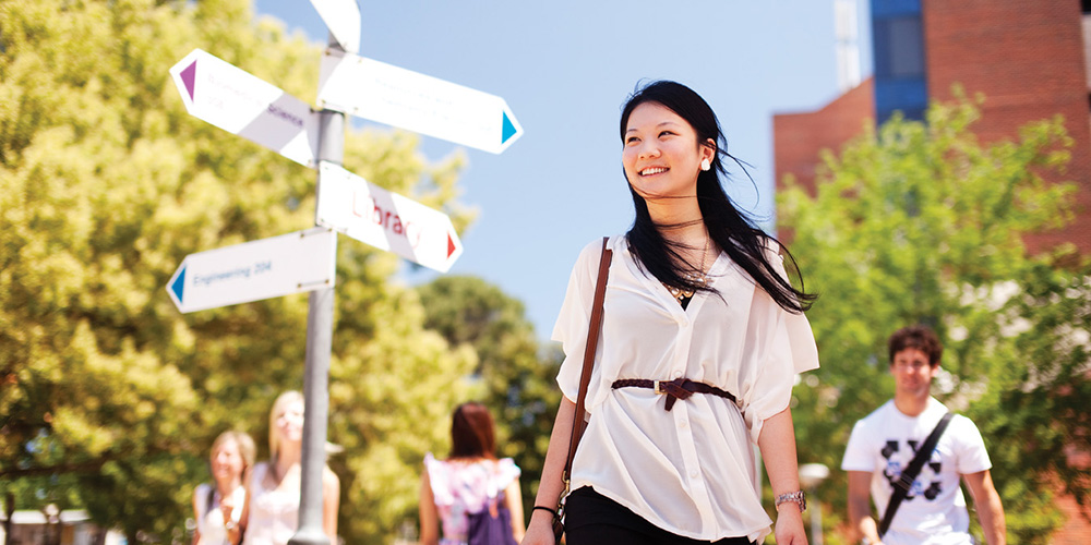 A female walking through the grounds at Curtin with a signpost in the background