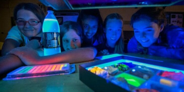 Young school aged students in the dark looking at glowing objects